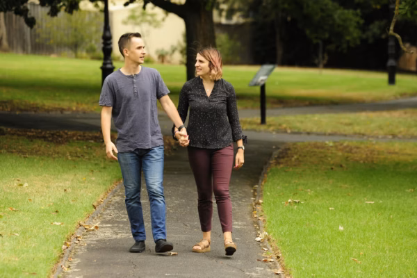 Young man and woman walking in park holding hands
