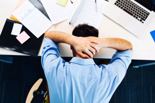 Man slumped over desk with hands on head